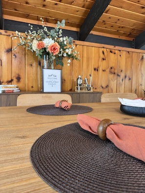 A wooden interior with a table set for dining, a vase with flowers, and a framed welcome sign. - Walk to Echo Lake • Sleeps 8 • Pet-Friendly Chalet (Conway)