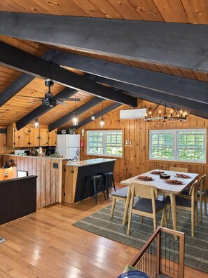 Una cocina rústica con paredes de madera, una isla central, taburetes de bar y una mesa de comedor con sillas.