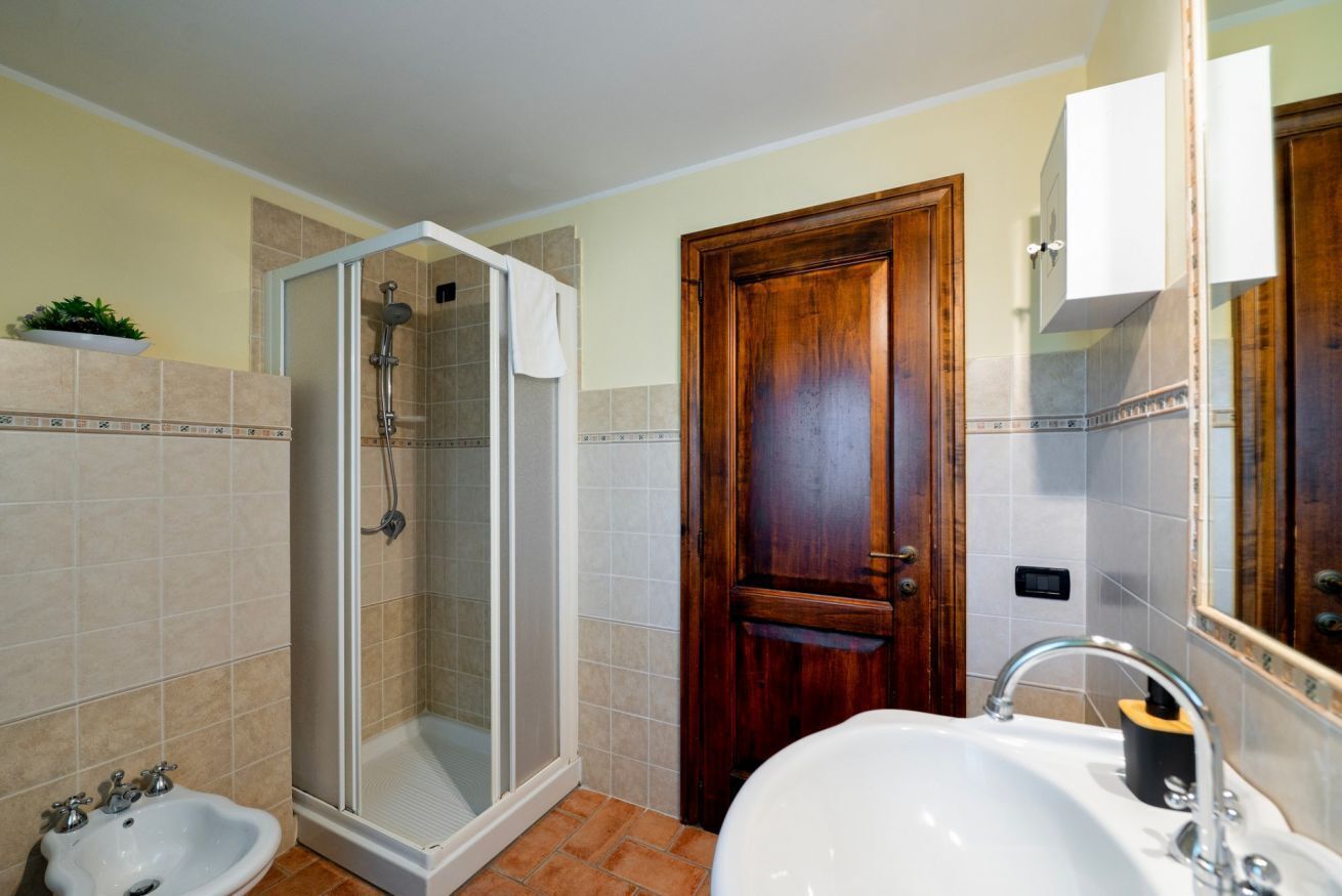 Een badkamer met een douche, wastafel en houten deur.