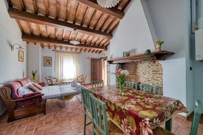 Ein gemütliches Wohnzimmer mit Holzboden, einem Esstisch mit blumigem Tischlein, einer Couch und Sesseln.
