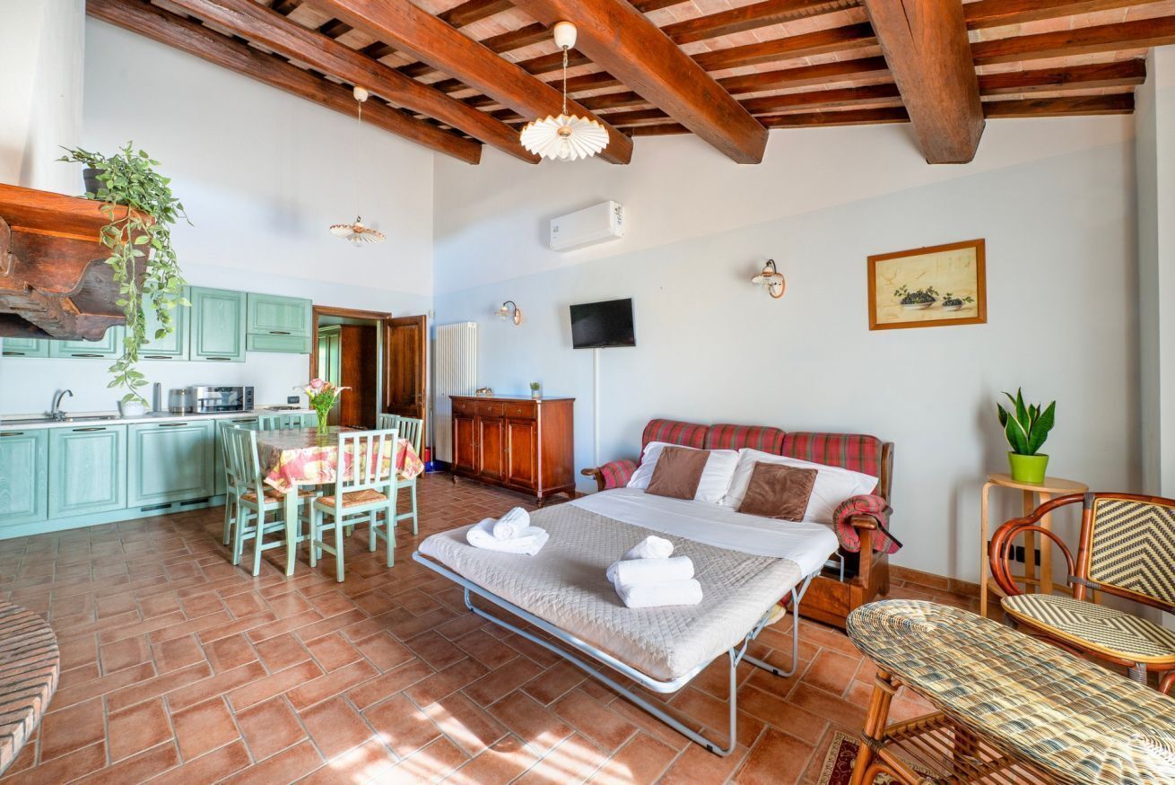 A room with a bed, a dining table with chairs, a kitchen area, and a large window.
