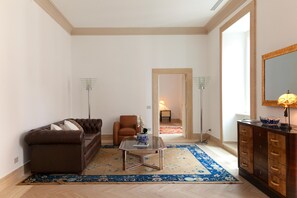 Ein Wohnzimmer mit einem braunen Sofa, einem Glastisch, einem blauen Teppich mit Muster, einem Holzschrank und einem Spiegel an der Wand.