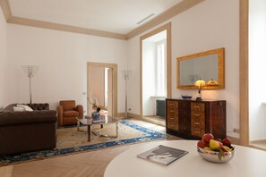 Ein Wohnzimmer mit einer Couch, einem Sessel, einem Couchtisch und einer Obstschale auf einem weißen Tisch.