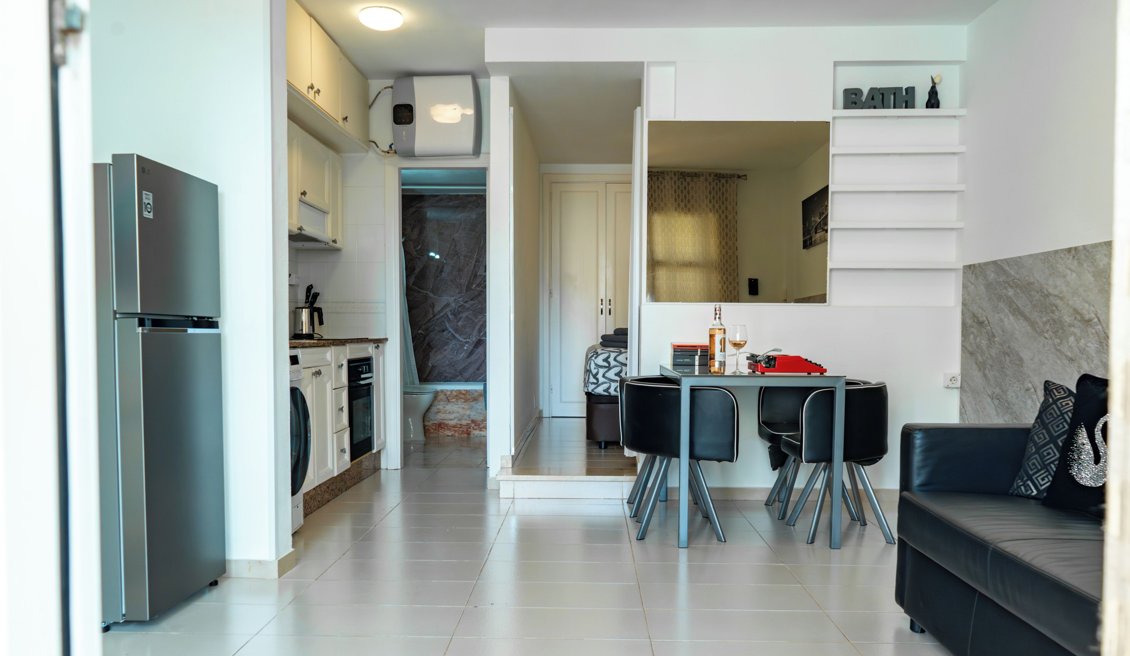 Una cocina moderna con refrigerador, horno y lavadora. Hay un comedor con una mesa y sillas, y un sofá en la sala.