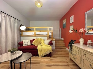 Une pièce comprenant un lit superposé, un canapé, une petite table, une commode et un miroir.