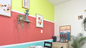 Un comedor con una mesa preparada para cuatro, sillas, una cafetera y adornos de pared, incluyendo un letrero con una nube de palabras y una fotografía enmarcada.