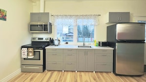 Cocina compacta con estufa, microondas, horno, refrigerador y ventana con vista a casas.