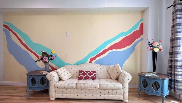 A room with a beige sofa, two side tables, a wall with abstract art, and a striped curtain. - HUGE 2 King Beds Family Home 3BR 3BA Sleeps 12 (Port Colborne)