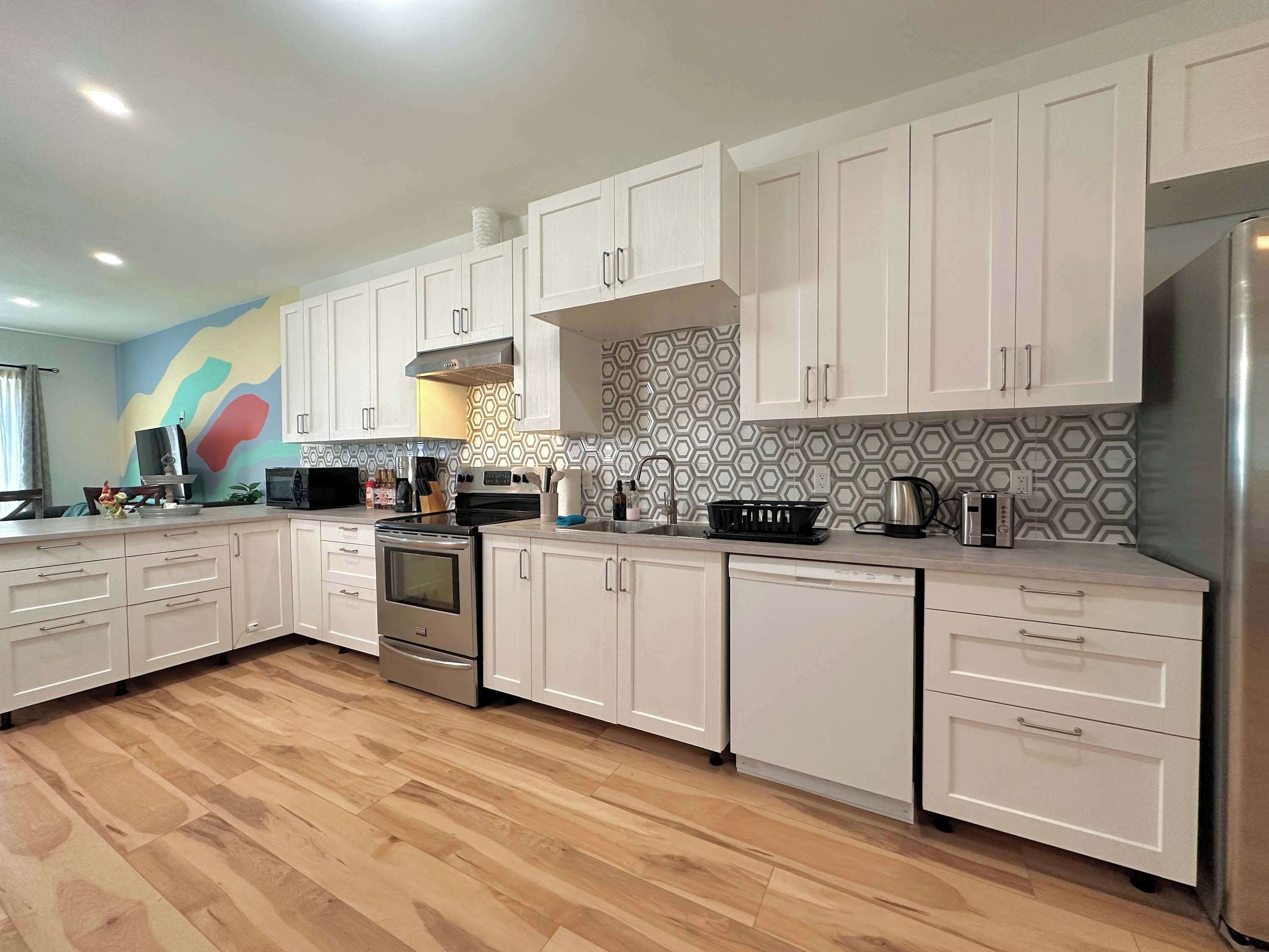 A modern kitchen with white cabinets, stainless steel appliances, and a colorful backsplash.