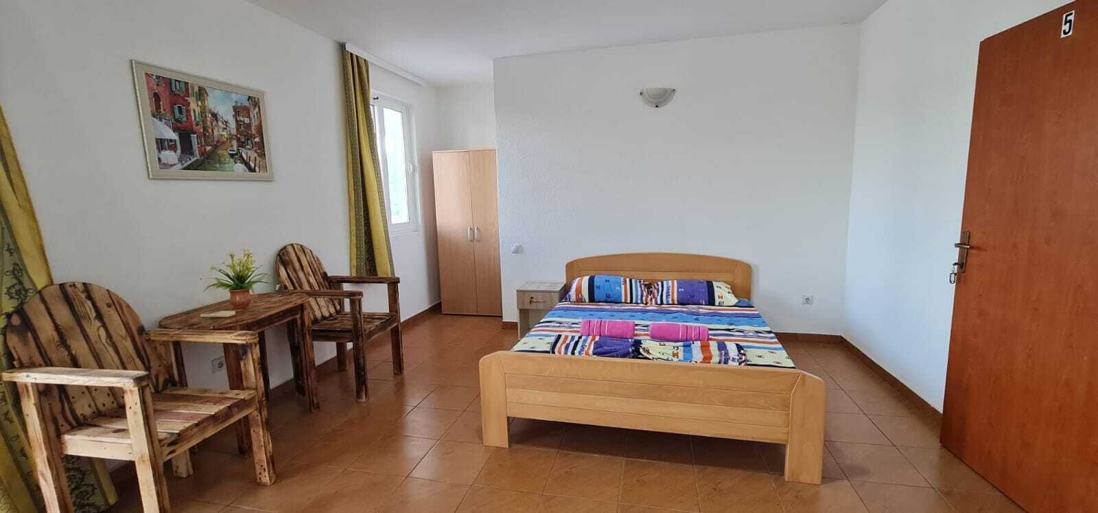 Une pièce comprenant un lit, un bureau en bois, deux chaises, une armoire et un tableau accroché au mur.