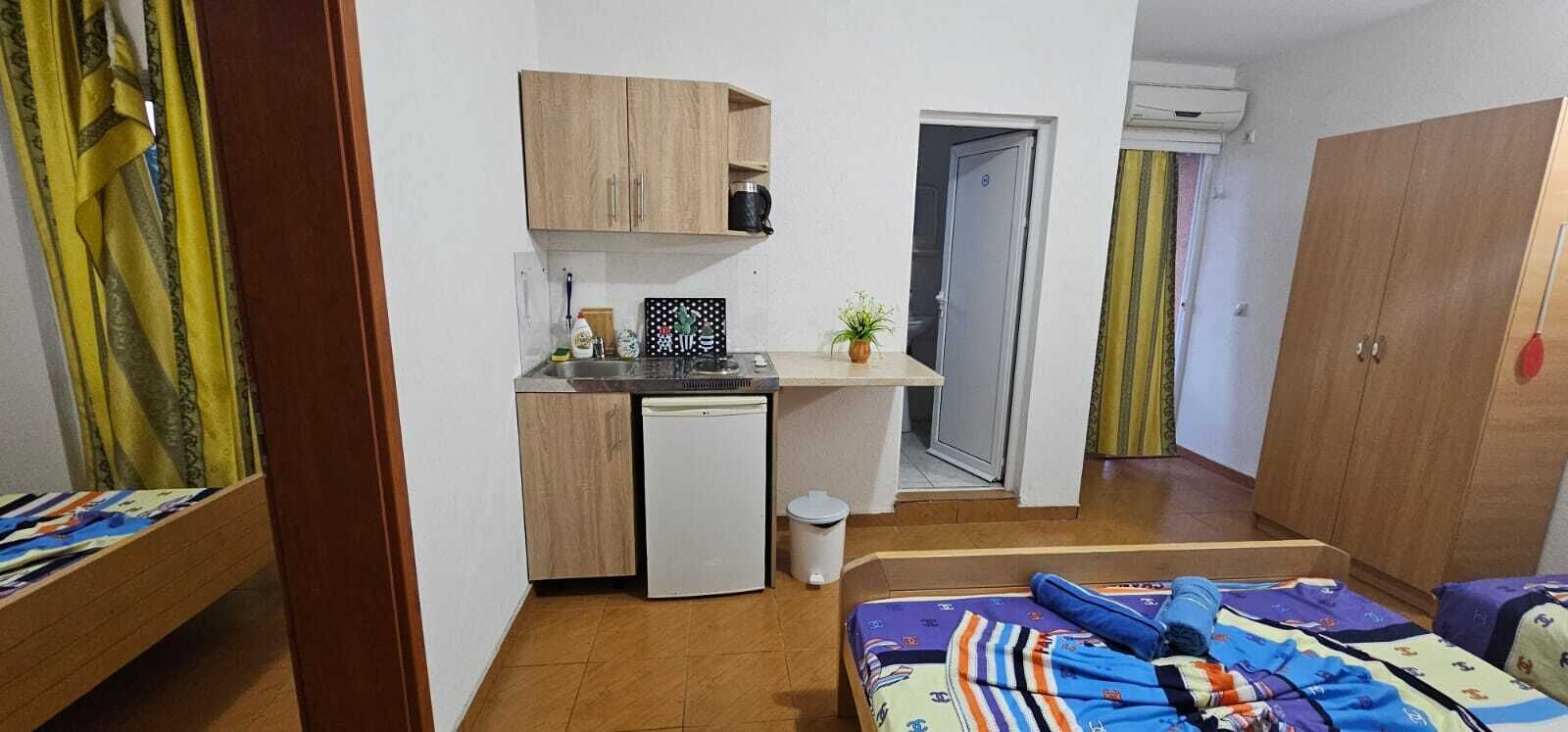 Une pièce compacte comprenant un coin cuisine, un lit avec une literie aux couleurs vives et une armoire.