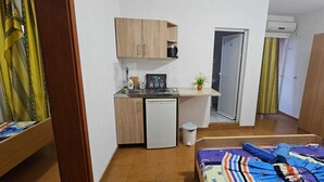 Pieni huone, jossa on pieni keittiönurkkaus, värikkäällä tekstiilillä varustettu sänky ja vaatekaappi.