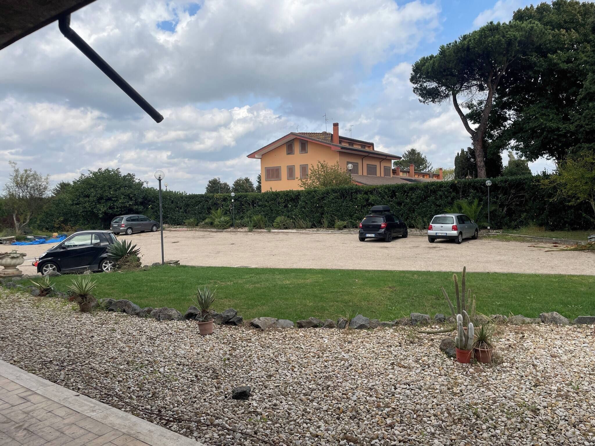 A parking area with three cars, a building with a yellow facade, and a well-maintained lawn with small plants and rocks.