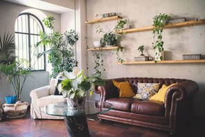 Uma sala de estar com um sofá de couro marrom, uma mesa de centro de vidro e várias plantas em vasos.