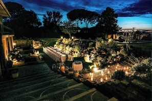 Um jardim com mesas e cadeiras, rodeado por plantas e velas.