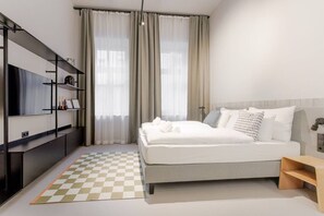 Ein modernes Hotelzimmer mit einem Bett, einem Fernseher, einem Bücherregal und einem karierten Teppich.