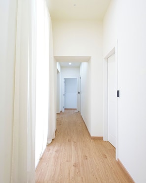 A hallway with wooden flooring, white walls, and doors.
