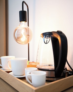 A coffee maker on a tray with cups, a clear glass, and a hanging light bulb.