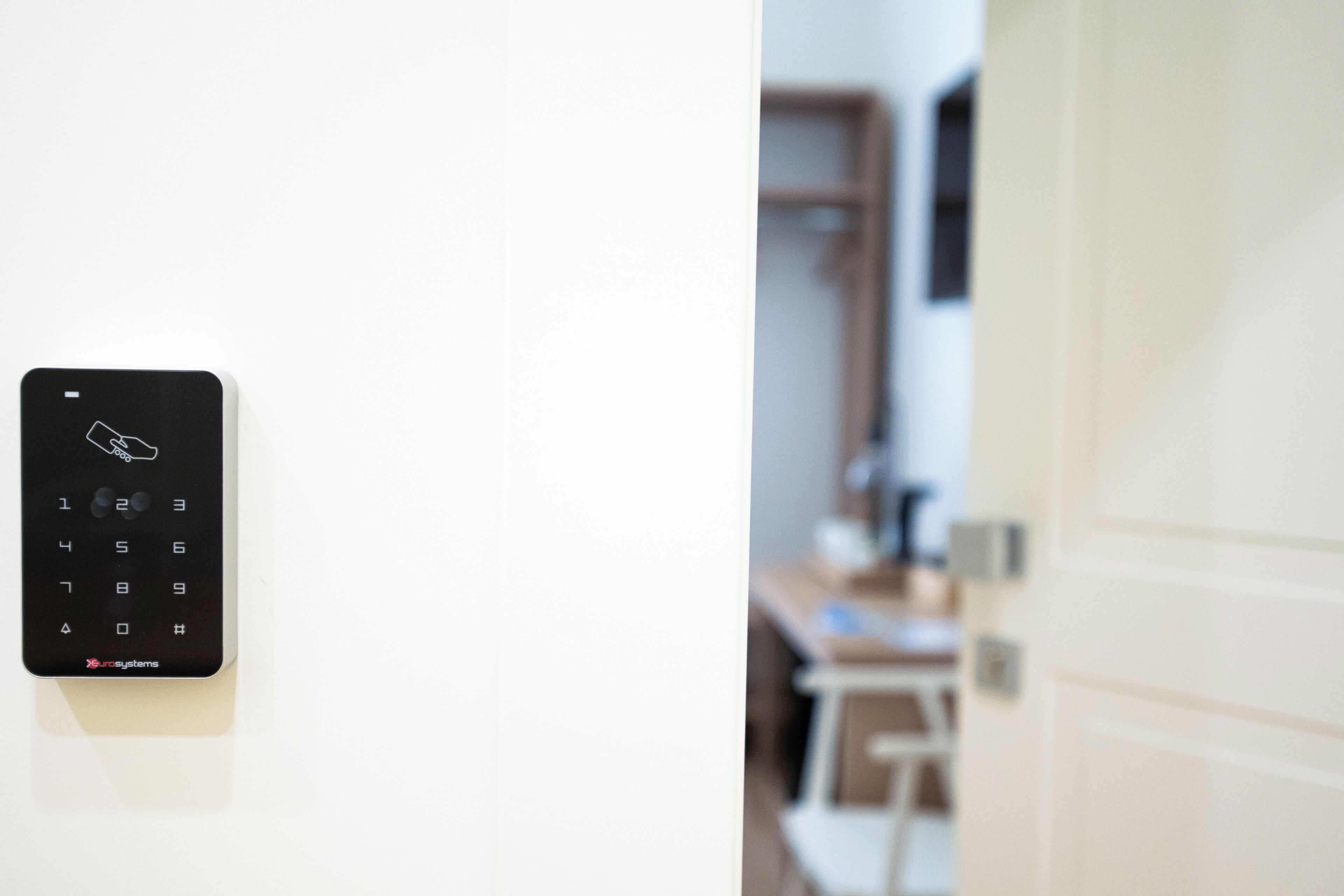 Cerradura de puerta con teclado y vista borrosa del interior de una habitación con un escritorio y armarios.