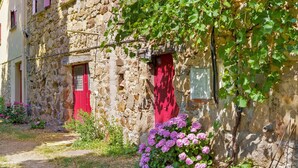 Ein Gebäude aus Stein mit roter Tür, Efeu und violetten Blüten.