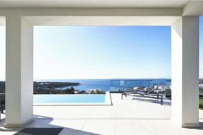 Eine moderne Terrassenanlage im Freien mit Pool, blauem Himmel und weiter Meerblick.