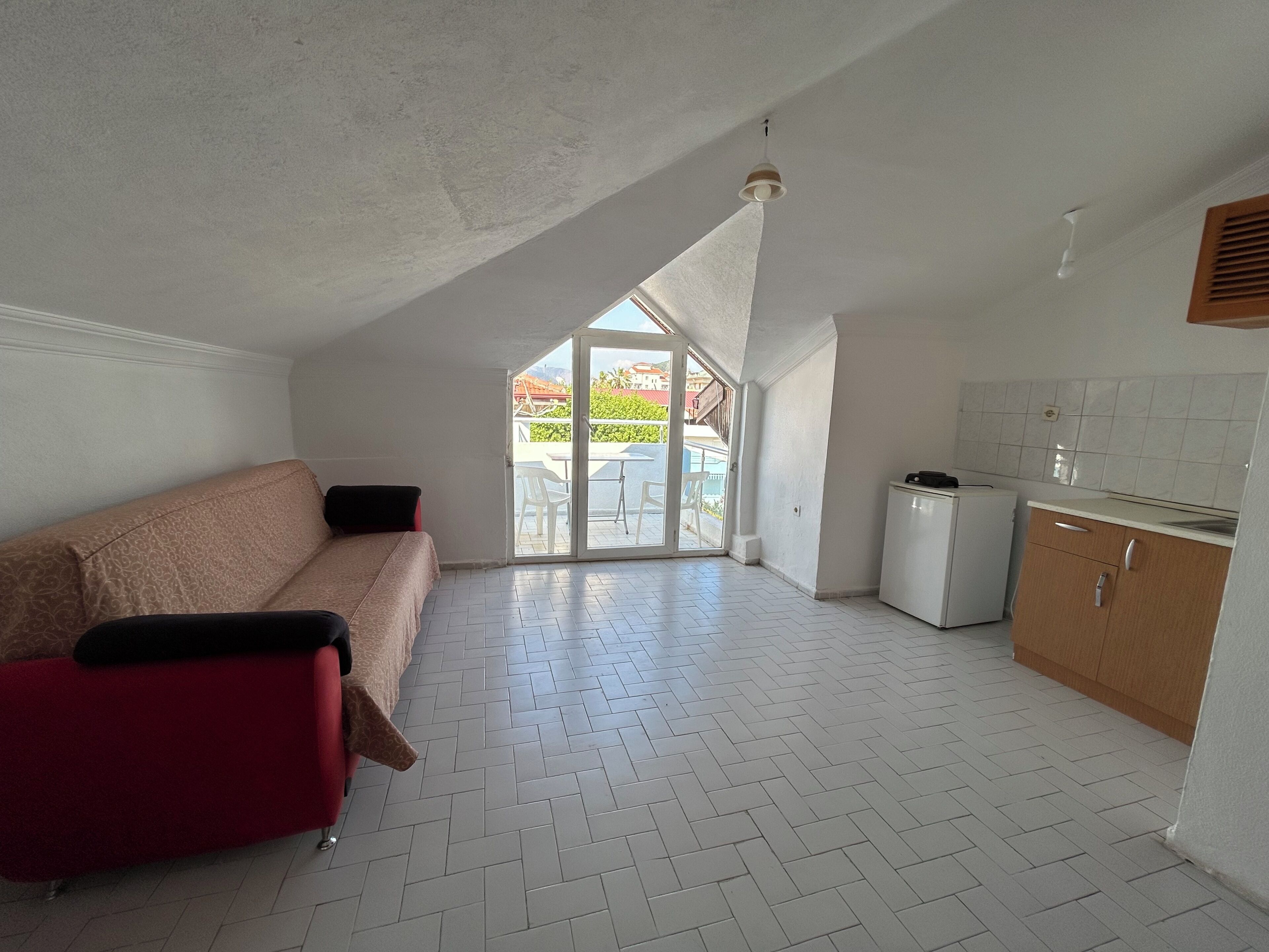 A compact living space with a kitchenette, a sofa, and a sliding glass door leading to an outdoor area.