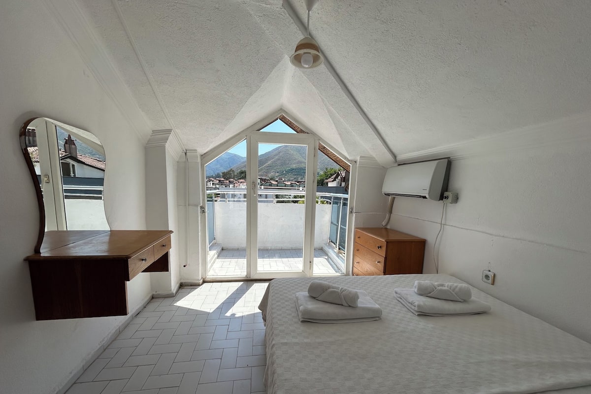 Une chambre à coucher avec un lit, une commode en bois, un miroir et une vue sur l’extérieur.