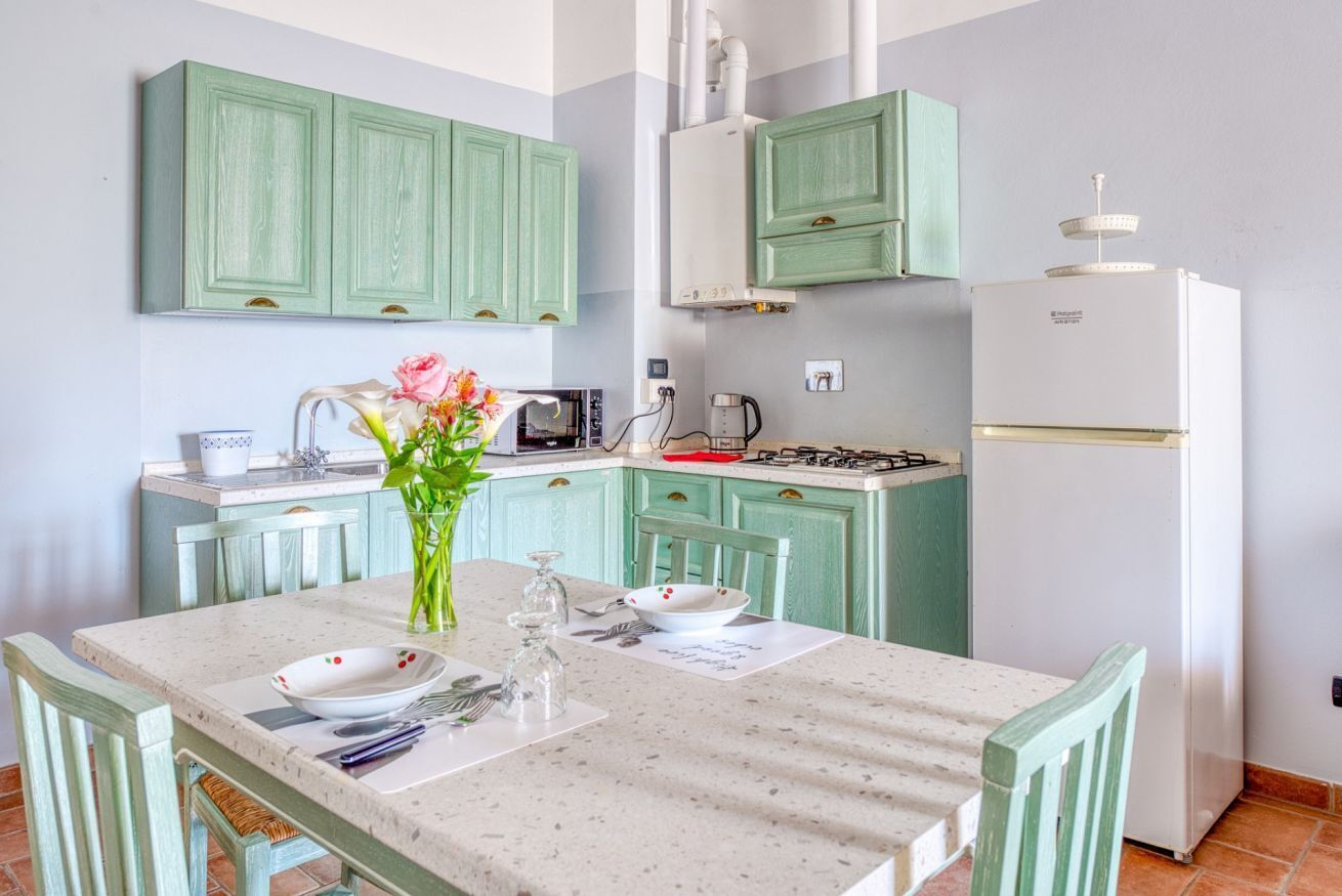 Una cucina con mobili color petrolio, un frigorifero bianco, un fornello a gas e un tavolo da pranzo con sedie.