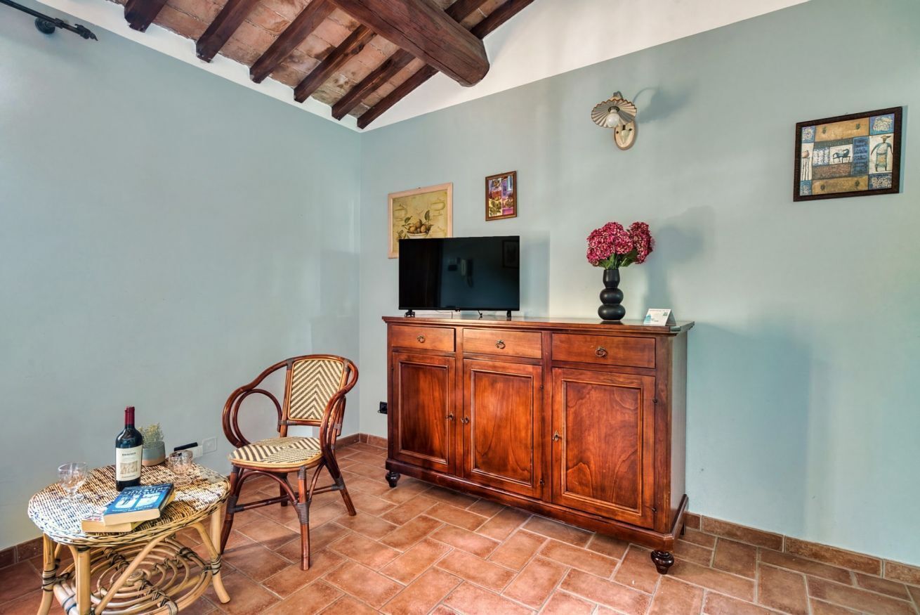 A room with a wooden cabinet, a television, a wicker chair, and a small table with a bottle and glasses.