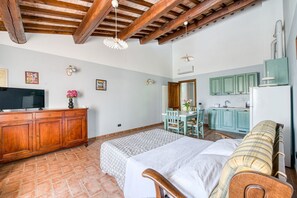 Ein Schlafzimmer mit einem Bett, einem Holz-Kopfende, einem Schminktisch, einem Fernseher und einer Küchenzeile mit Schränken und einem Kühlschrank.