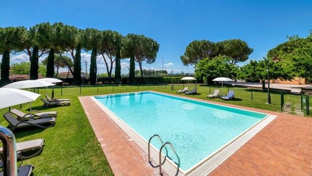 A rectangular swimming pool with a tiled edge, surrounded by a brick patio. There are lounge chairs and umbrellas along the poolside. - A charming 65 sqm apartment, ideal for four people, located on the first floor of a building without an elevator.The apartment is located in a charming Umbrian-style farmhouse, with ample green space, relaxation areas, and a shared swimming pool. Its loc (San Martino In Campo)