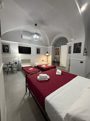Una camera d'albergo con un letto grande, due letti più piccoli, una scrivania con una sedia, una televisione e opere d'arte alle pareti.