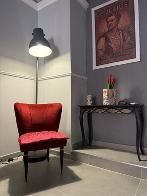 A red chair, a floor lamp, a console table with decorative items, and a poster on the wall. - Centurioni Tourist Accommodation (Civitavecchia)