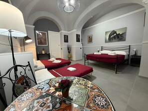A room with two beds, a table with a colorful pattern, and a large window with a view. - Centurioni Tourist Accommodation (Civitavecchia)
