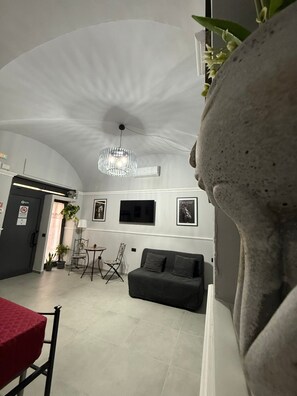 A modern living room with a curved ceiling, a chandelier, a sofa, a dining table, and a TV mounted on the wall. - Centurioni Tourist Accommodation (Civitavecchia)