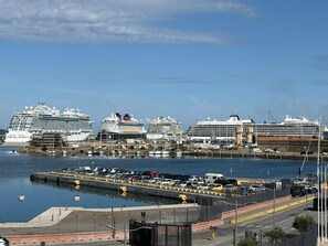 Un port de plaisance où sont amarrés plusieurs navires de croisière, un parking rempli de voitures et un ciel dégagé.