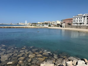 Una zona costiera con acque limpide, un litorale roccioso e edifici sullo sfondo.
