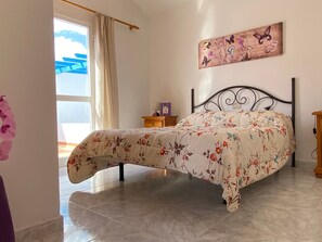 Een slaapkamer met een bed, nachtkastje, gordijnen voor het raam en een schilderij aan de muur.