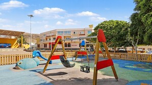 Un'area giochi con altalene e scivoli, circondata da edifici e alberi.