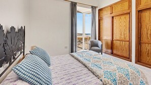 Una camera da letto con un letto, una sedia, una finestra con tende e un armadio in legno.