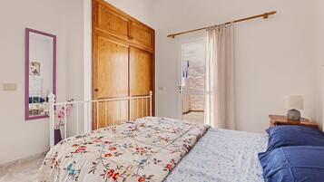 Una camera da letto con un letto, un armadio in legno, uno specchio, un comodino con una lampada e vista all'esterno da una finestra.