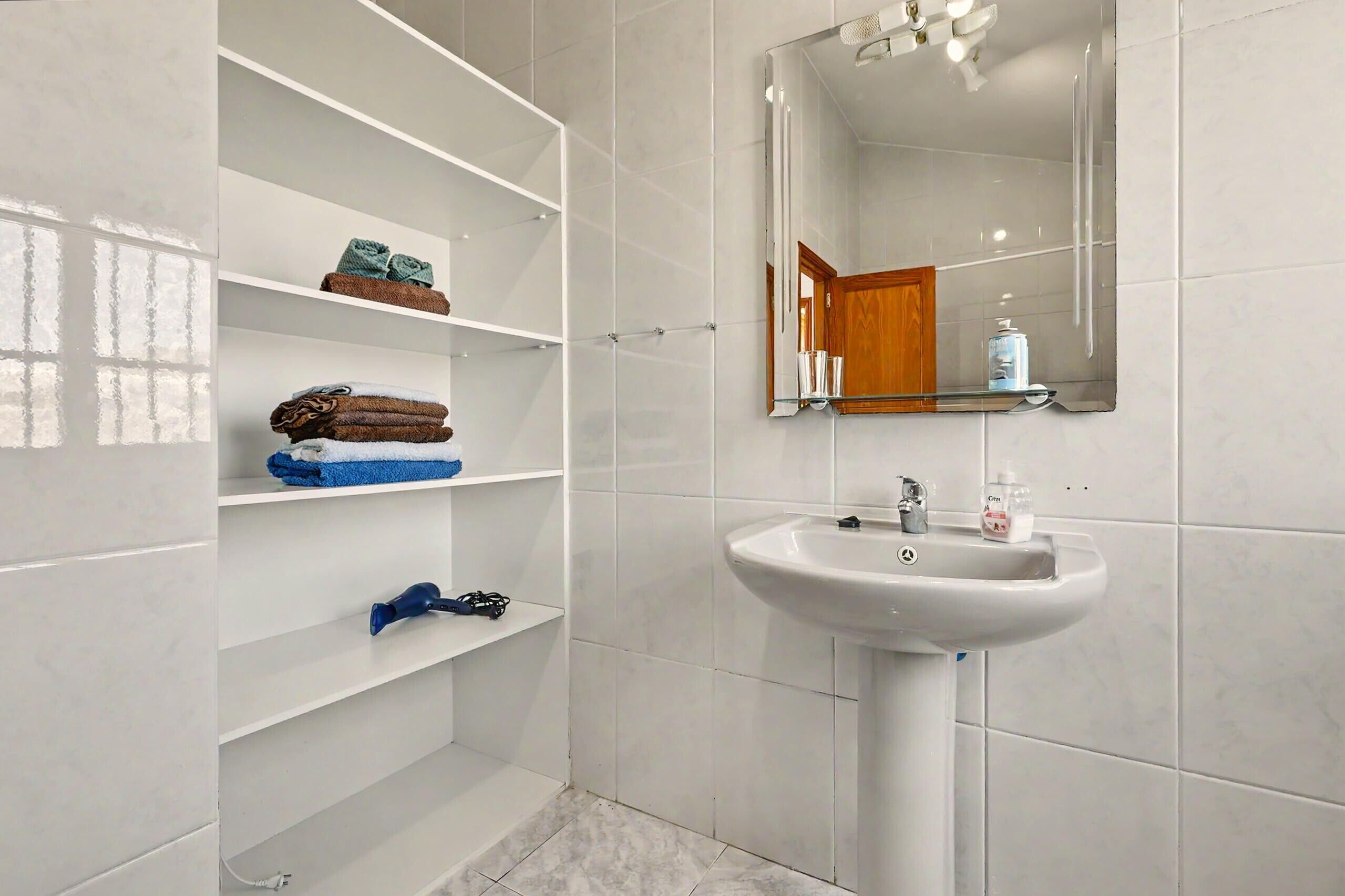 Un bagno con un lavandino bianco, uno specchio e mensole con asciugamani.