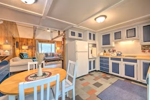 A compact kitchen with white cabinets, a dining table with chairs, and a living area with a sofa and a fireplace. - Cozy Bear Cabin / Trails, Firepit & Northern MI (Kalkaska)