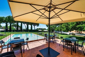 Eine Poolterrasse mit Sitzgelegenheiten und einem großen Sonnenschirm.