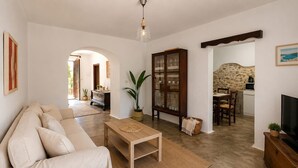 Una sala de estar con sofá, una mesa de centro de madera, un aparador con puertas de cristal, televisor y pared de piedra.