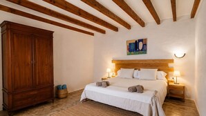 Un dormitorio con cabecera de madera, un armario grande, cama con ropa de cama blanca, dos lámparas de noche y un cuadro en la pared.