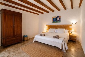 Ein Schlafzimmer mit einem hölzernen Kopfende, einem großen Kleiderschrank, einem Bett mit weißer Bettwäsche, zwei Nachttischlampen und einem Bild an der Wand.