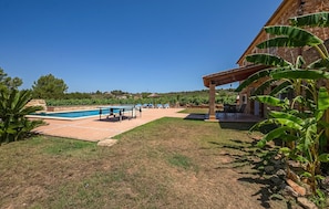 Ein Swimmingpool mit Liegestühlen, eine überdachte Terrasse und ein Steinhaus mit Garten.
