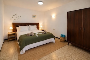 Ein ordentlich gemachtes Bett mit grüner Decke, zwei Nachttischlampen, einem Holzschrank und einer kleinen Wanddekoration.