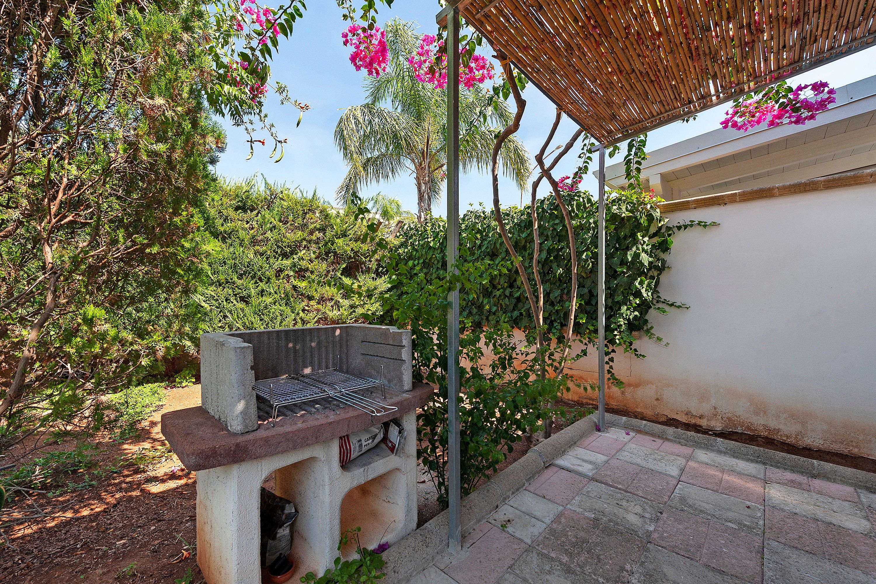 Una parrilla para barbacoa montada al aire libre, con una pérgola arriba.